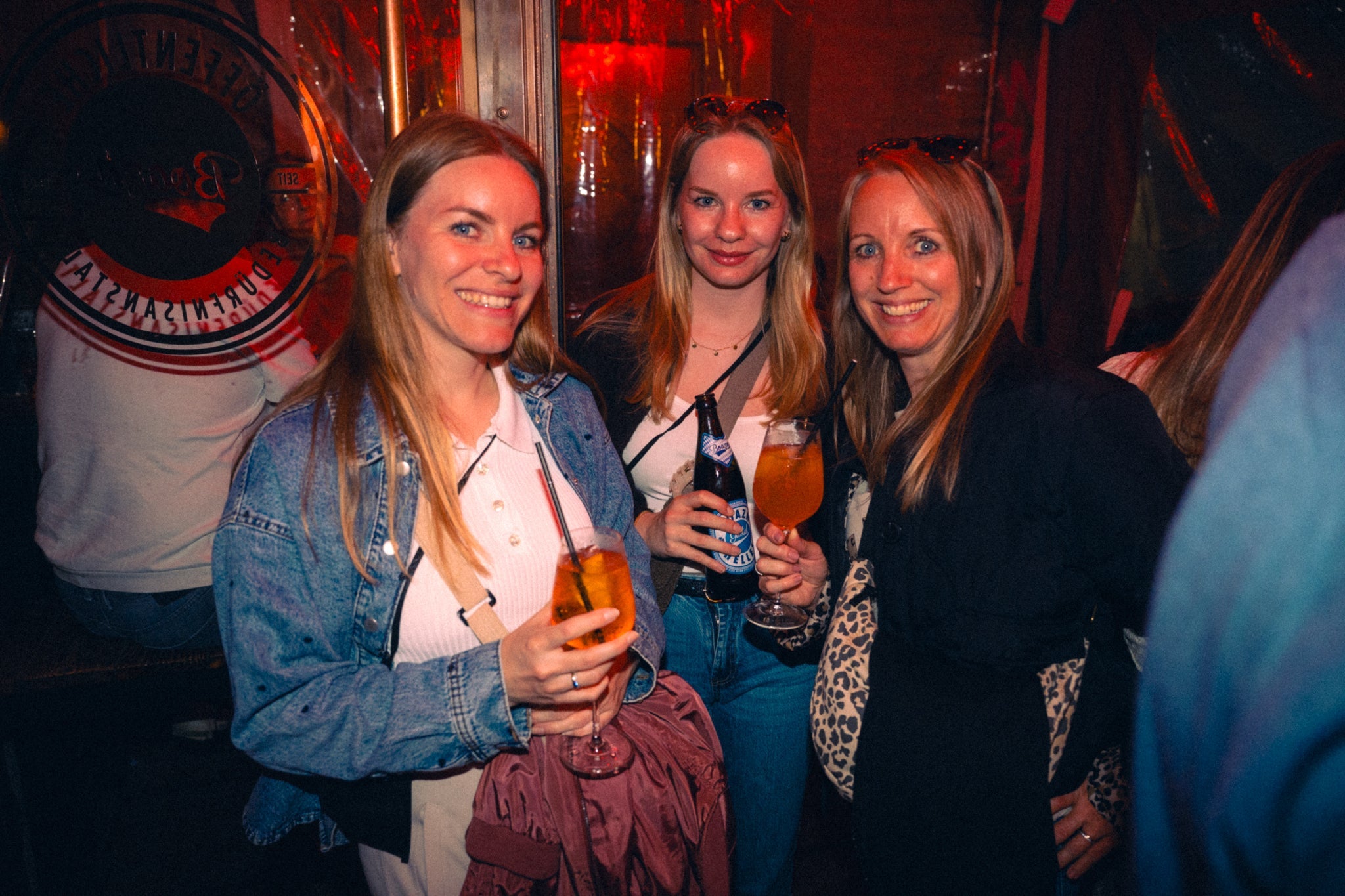Mädelsrunde mit Aperol-Drinks in der Boazn München vor Bedürfnisanstalt-Logo — Oktoberfest-Tipp authentische Münchner Bars