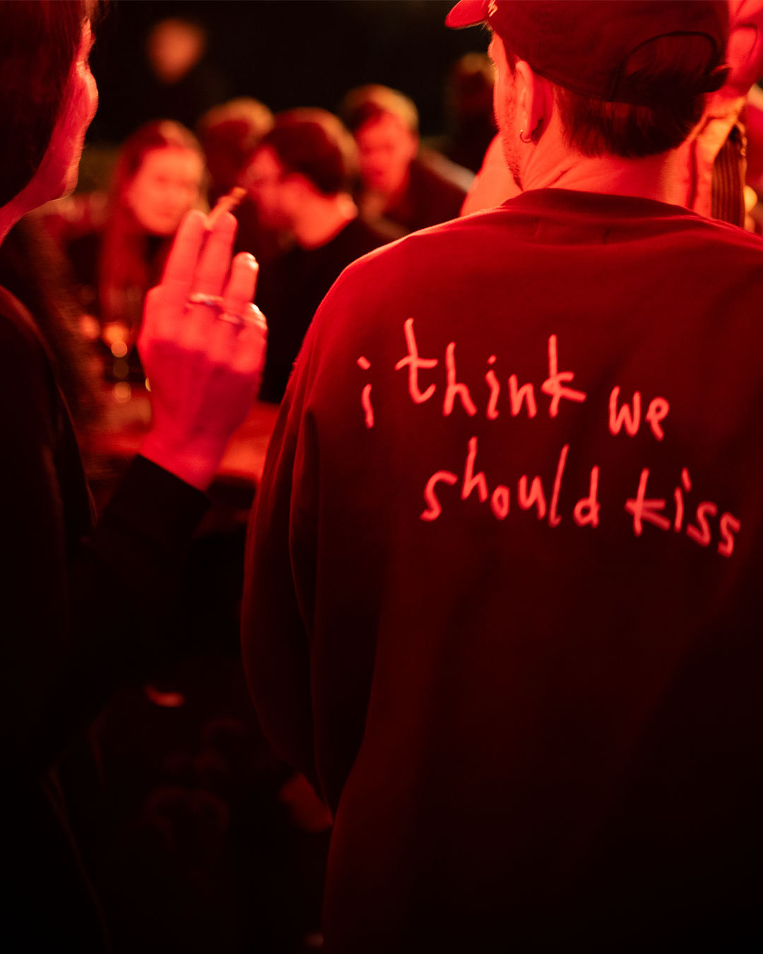 Gast von hinten im roten Sweatshirt mit Aufdruck „i think we should kiss“, daneben Frau mit Zigarette – Kneipe in München, Februar 2026 9
