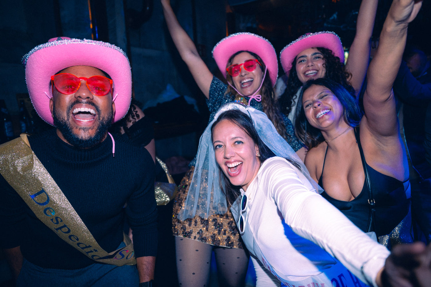 JGA-Gruppe mit pinken Cowboyhüten, Braut mit Schleier macht Selfie auf der Tanzfläche – Tanzbar an der Isar, März 2026 7