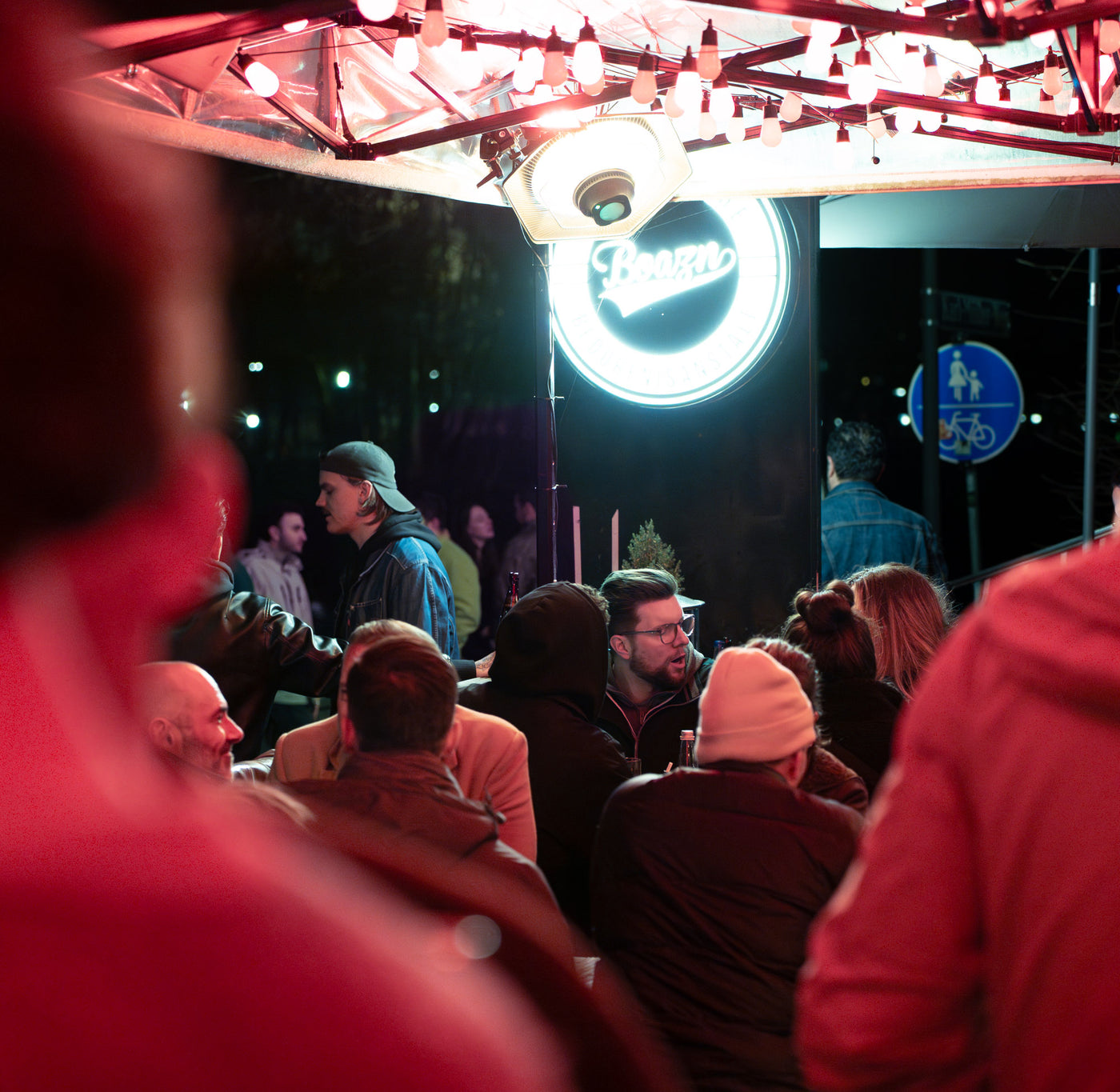 Boazn-Neon-Logo leuchtet über der Terrasse, Gäste sitzen unter roten Lichterketten – Tanzbar an der Isar, Januar 2026 4