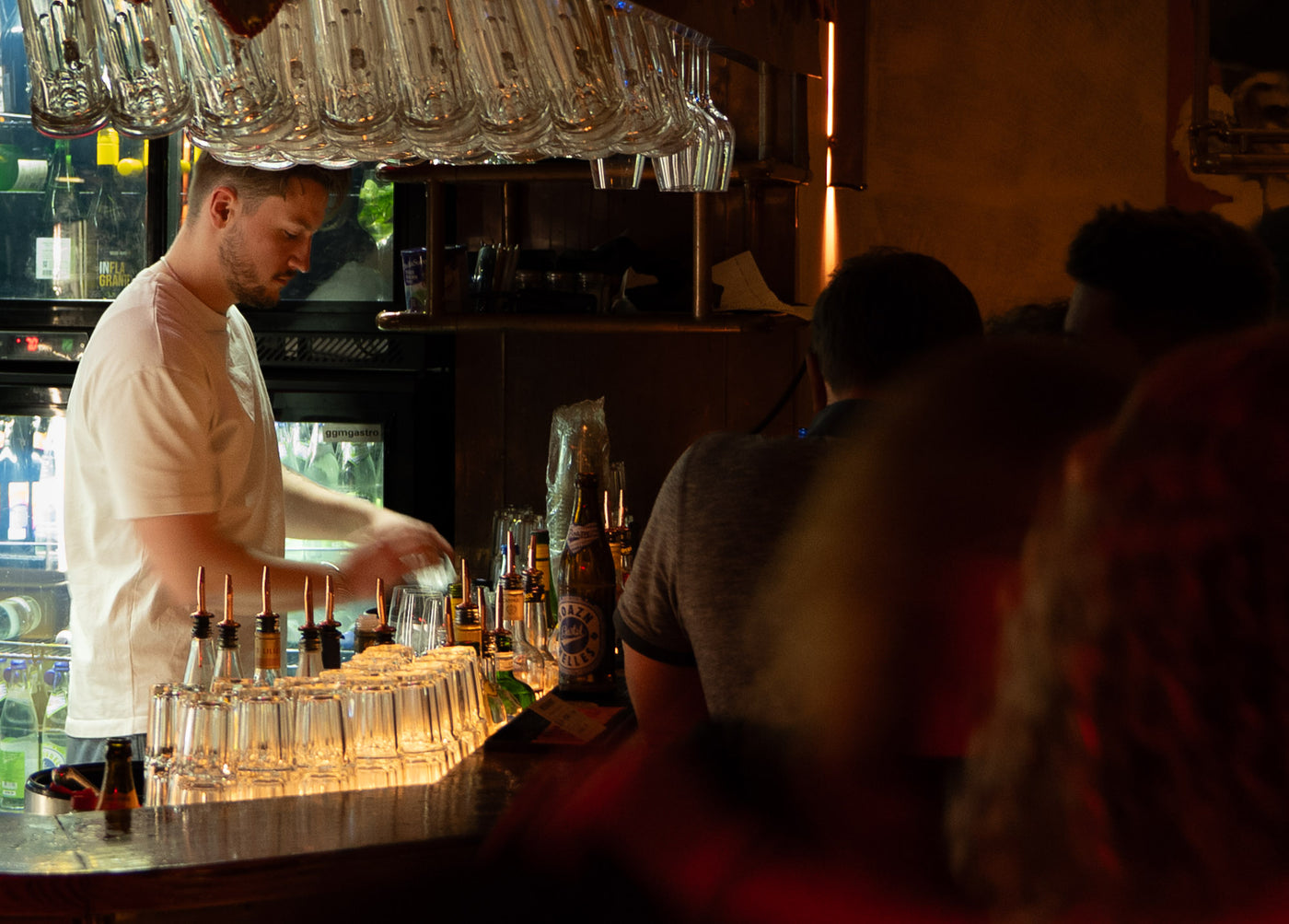 Barkeeper im weißen T-Shirt mixt Drinks unter hängenden Weingläsern – Bar an der Ludwigsbrücke, Januar 2026 6