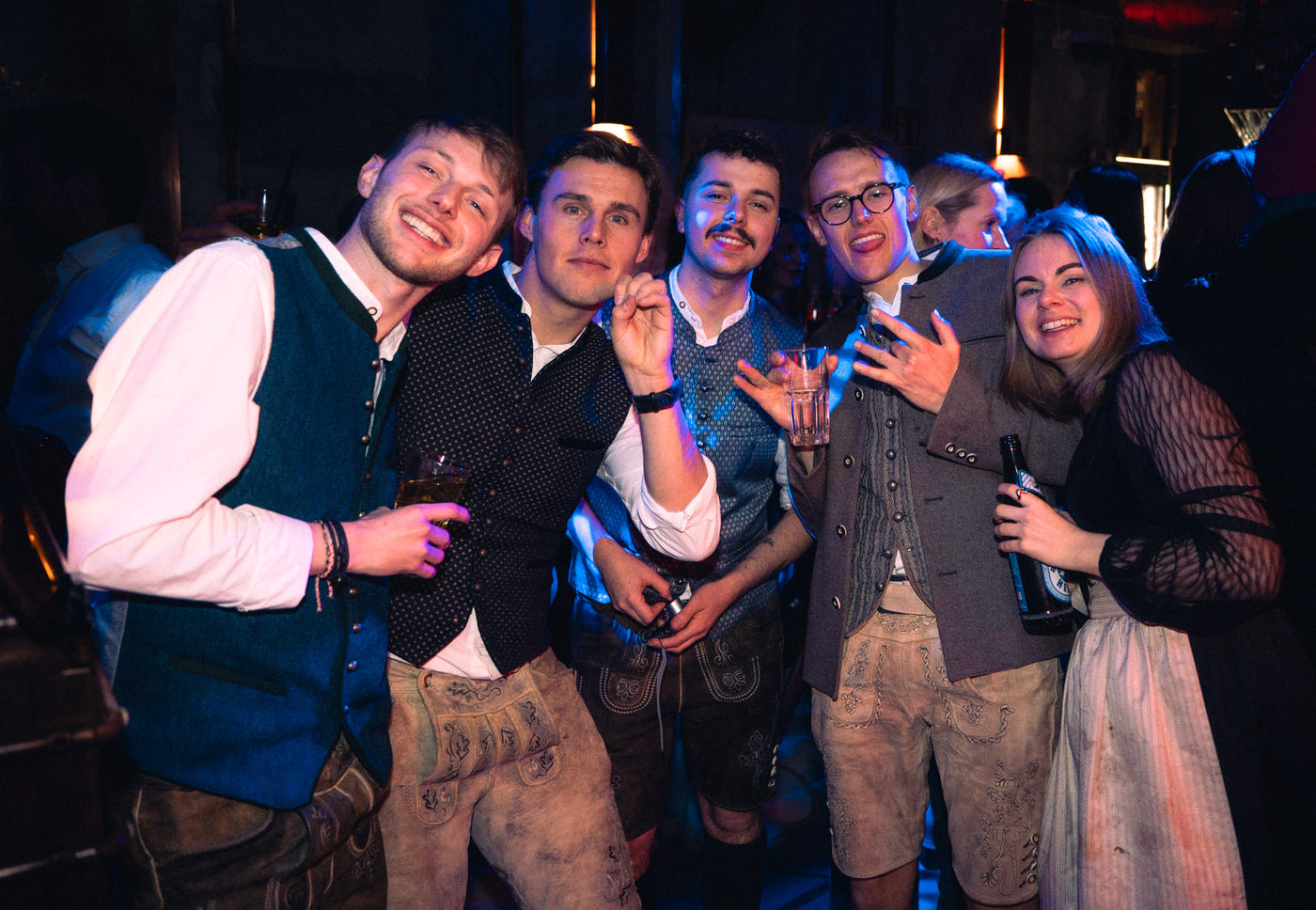 Fünf Freunde in Lederhosen und Trachtenwesten posieren lachend nebeneinander – Tanzbar in München, Februar 2026 23