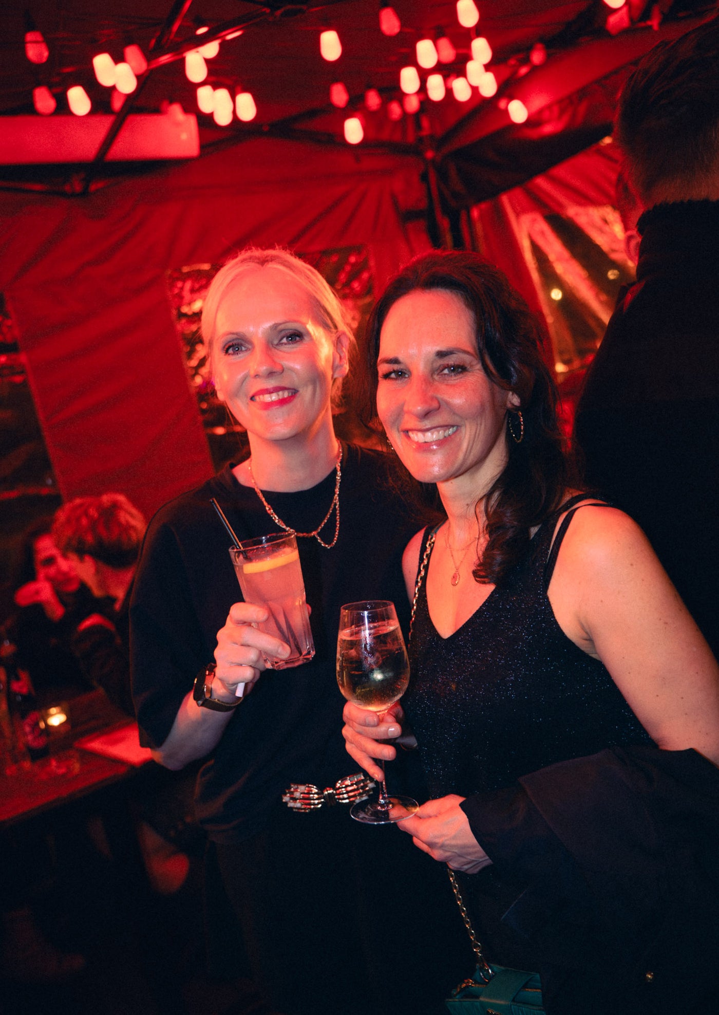 Zwei elegante Frauen in Schwarz mit Aperol-Spritz und Weißwein unter Lichterketten – Tanzbar an der Isar, Februar 2026 27