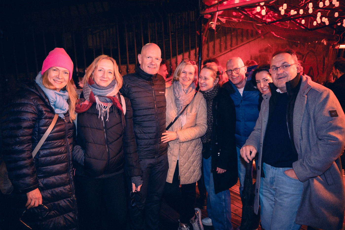Achtköpfige Gruppe in Winterjacken posiert lachend vor warm beleuchteter Boazn-Terrasse – Tanzbar an der Isar, Januar 2026 10