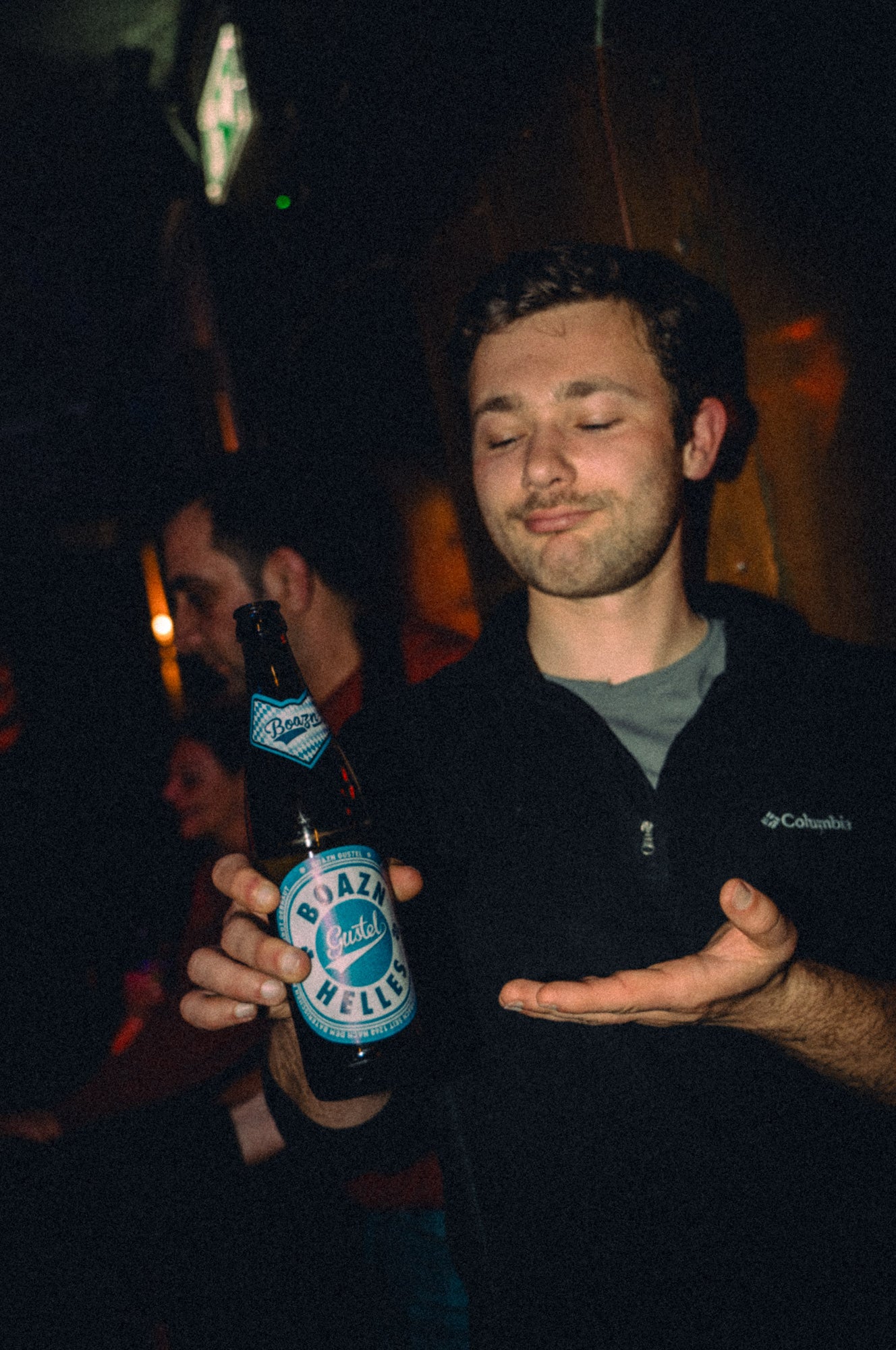 Junger Mann präsentiert stolz eine Flasche Boazn-Gustel-Helles in die Kamera – Eigenbier der Boazn, München, März 2026 11