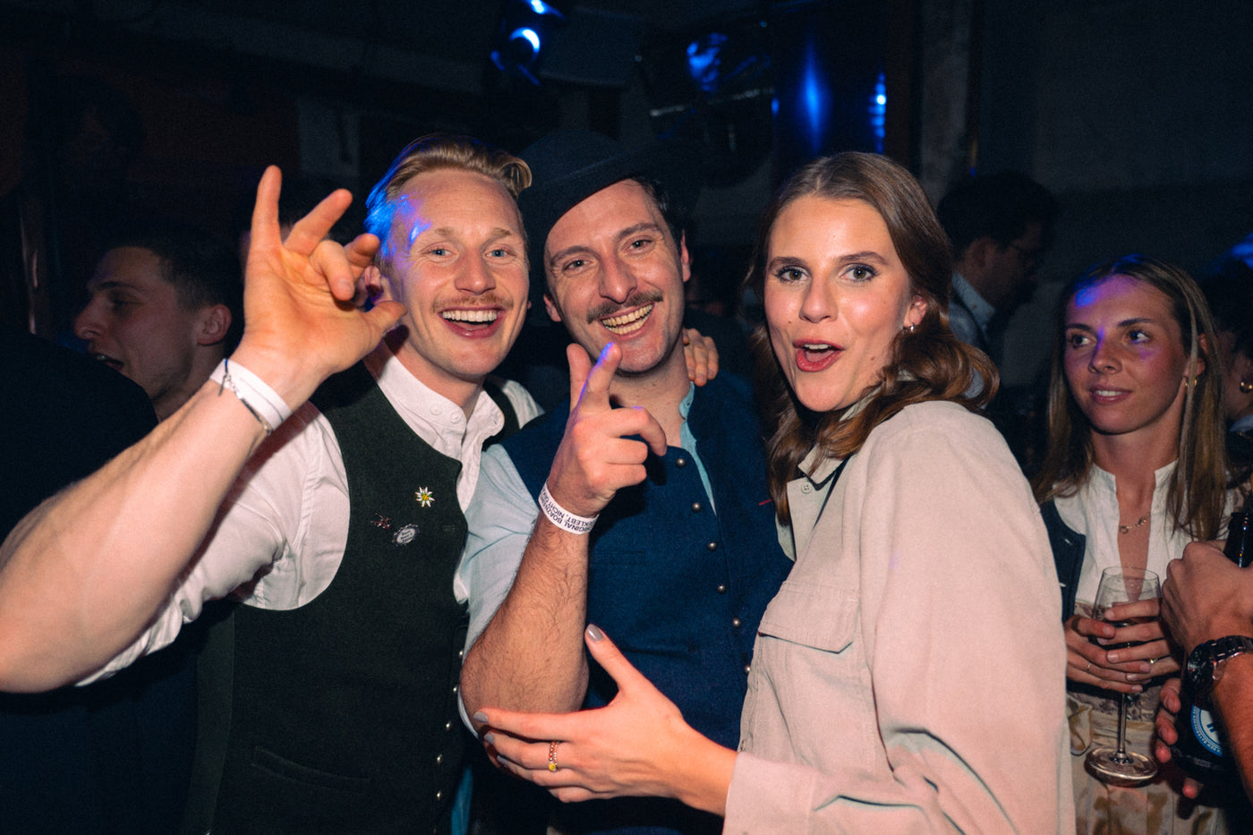 Drei Freunde in Trachtenwesten und mit Hut lachen ausgelassen, eine Frau zeigt zur Kamera – Nightlife München, Februar 2026 6