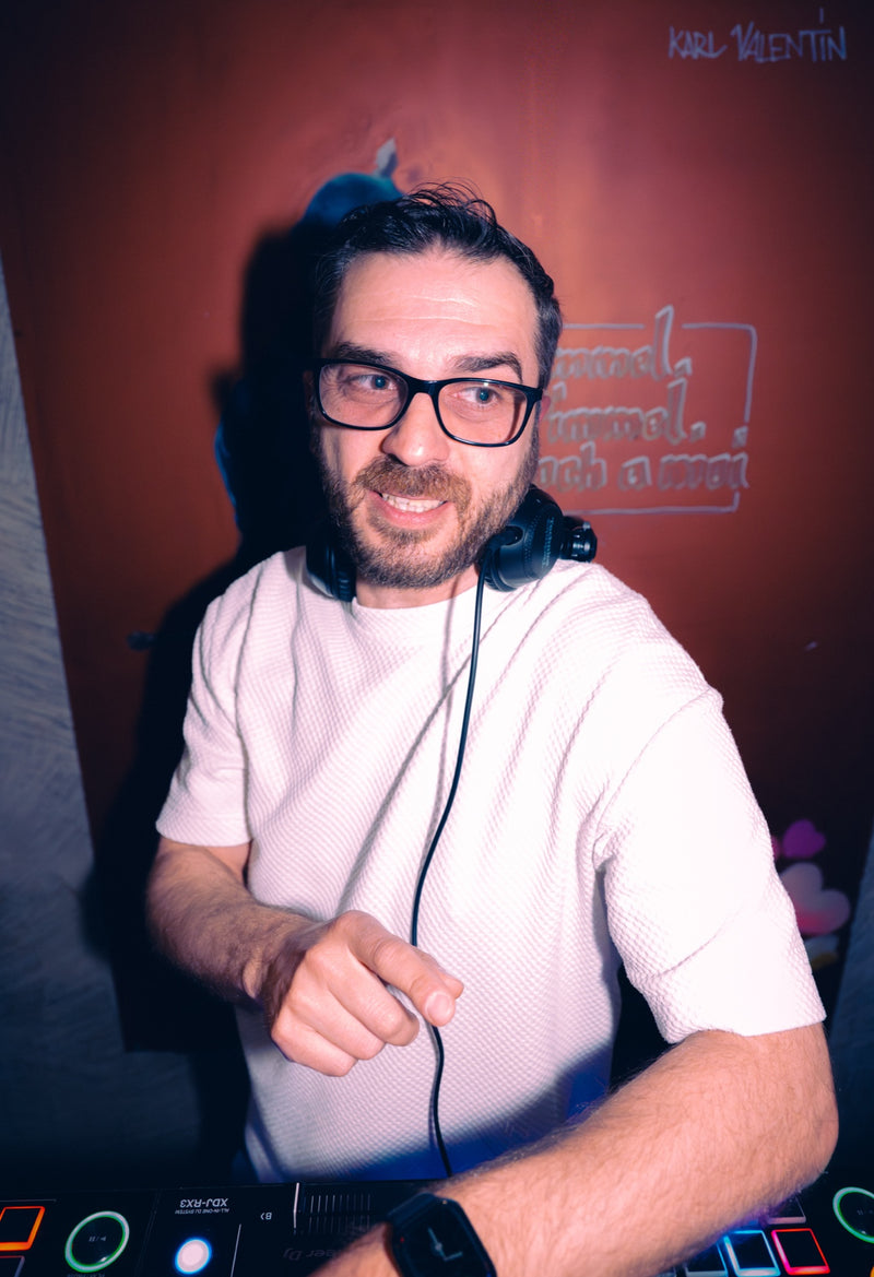 Aleks, Resident-DJ der Boazn München, mit Brille und Kopfhörern am DJ-Pult