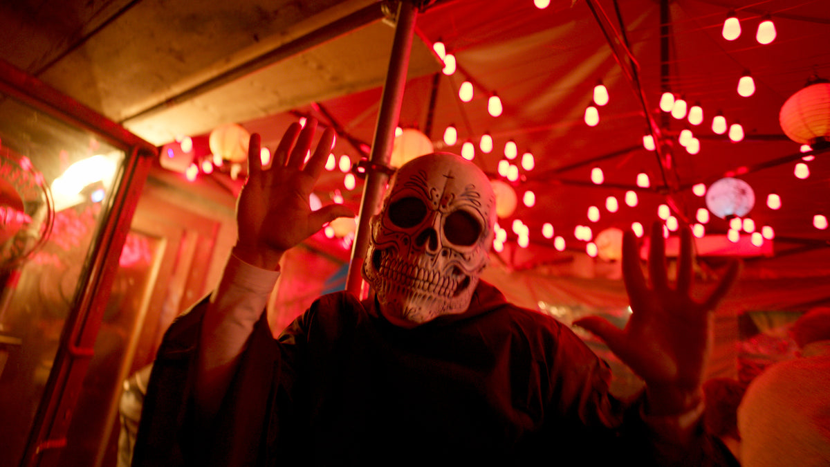 Gast mit Sugar-Skull-Maske hebt die Hände unter roten Lichterketten – Halloween 2025 in der Boazn München