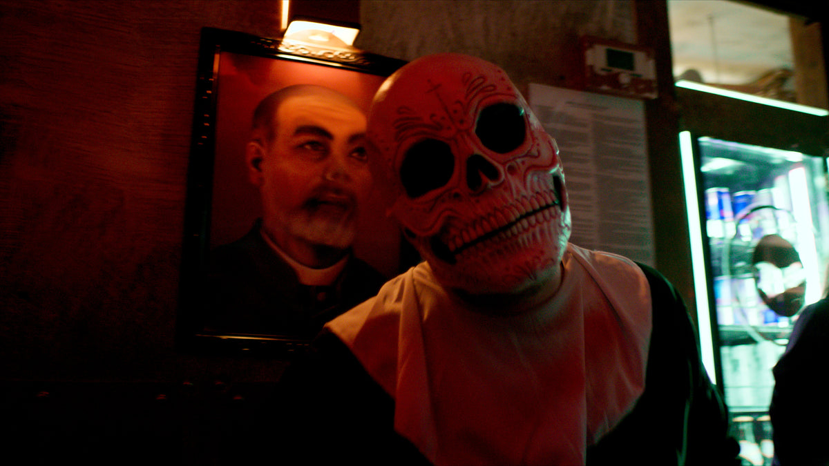 Gast mit Sugar-Skull-Maske neben einem gerahmten Wandbild – Halloween 2025 in der Boazn München 3
