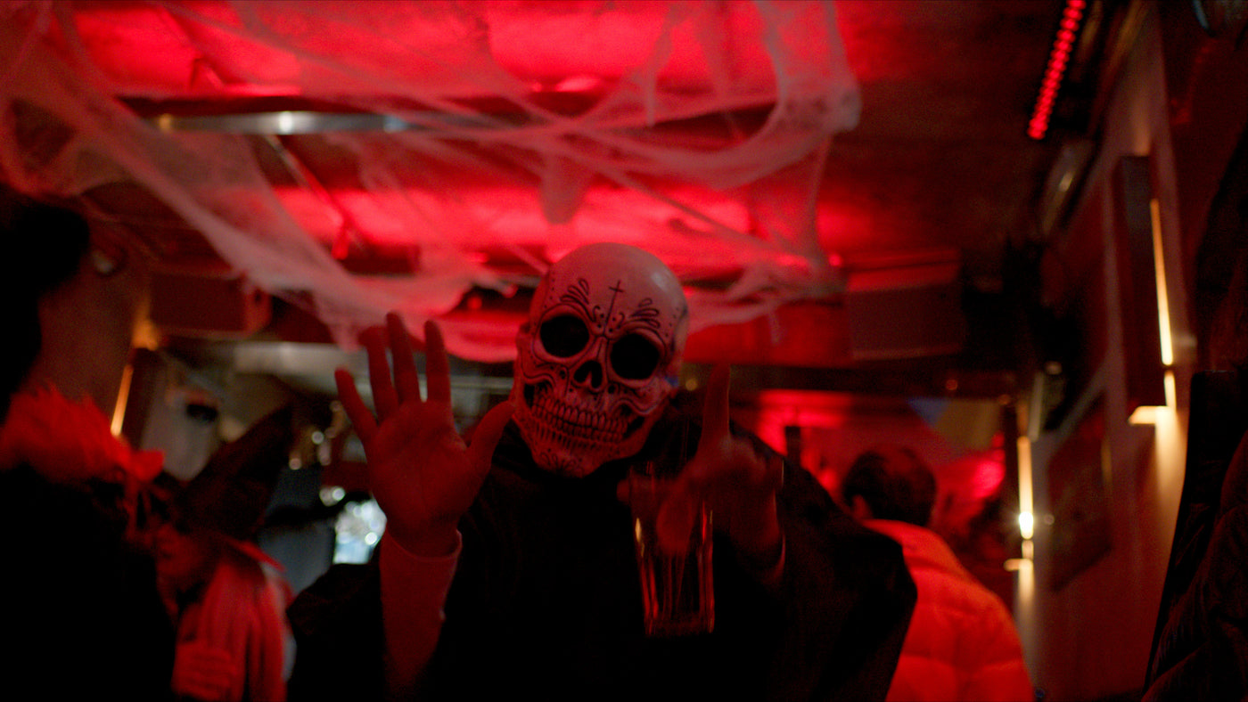 Gast mit Sugar-Skull-Maske und Bier unter Deko-Spinnweben – Halloween 2025, Bar an der Ludwigsbrücke 9