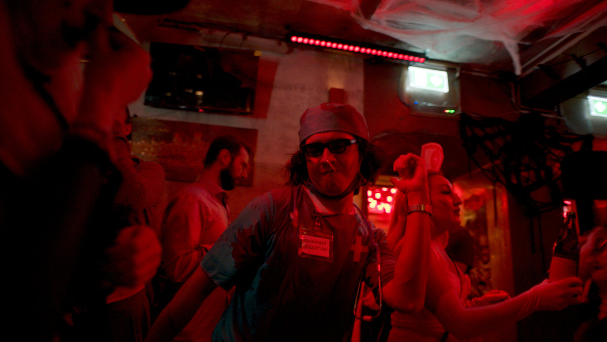 Gast im blutigen Arztkittel mit OP-Haube und Sonnenbrille – Halloween 2025, Bar an der Ludwigsbrücke 17