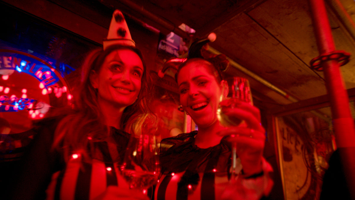 Zwei Gäste heben ihre Gläser neben dem Boazn-Leuchtschild – Halloween 2025, Bar in München 49