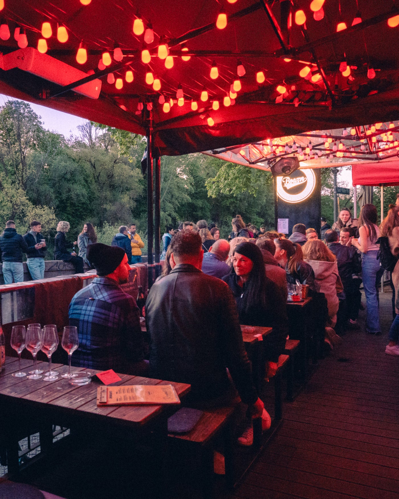 Volle Terrasse mit Lichterketten und leuchtendem Boazn-Logo am Isar-Ufer – München, April 2026 4