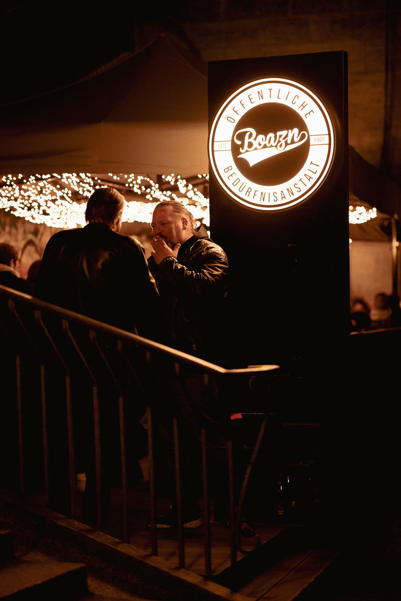 Beleuchtetes Boazn-Logo am Eingang bei Nacht – Bar unter der Ludwigsbrücke, München, Dezember 2025