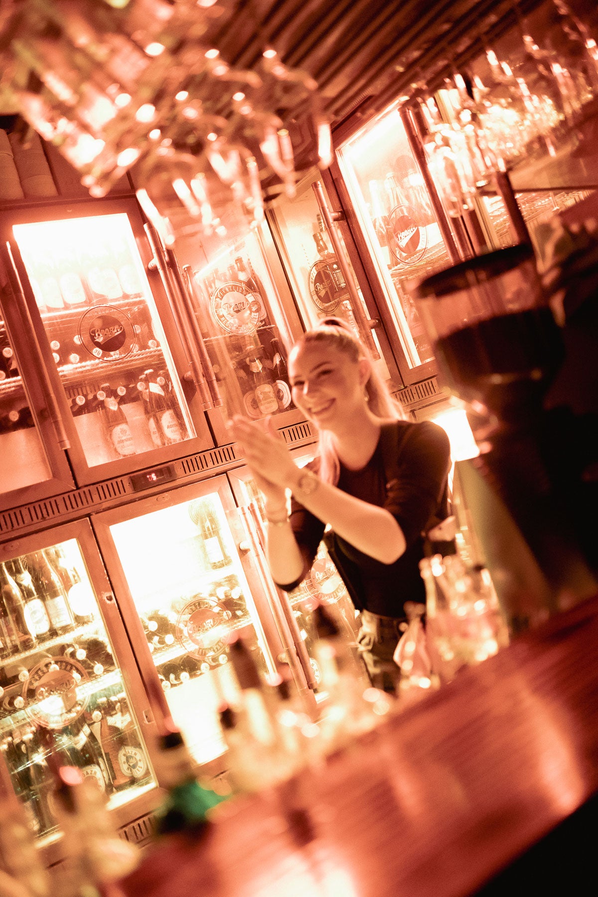 Bartenderin lacht hinter dem Tresen vor leuchtendem Kühlschrank – Boazn München, Bar an der Isar, Dezember 2025 39