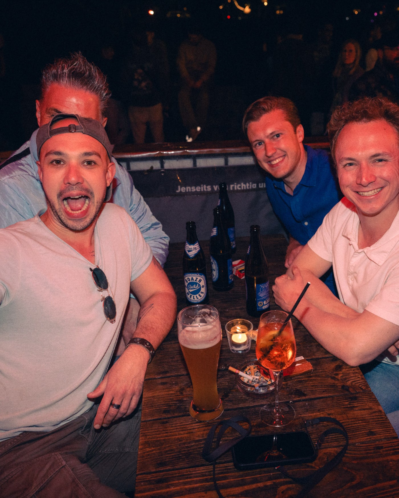 Vier Freunde stoßen am Holztisch mit Boazn Helles und Weißbier an – Boazn München, Bar an der Ludwigsbrücke, Mai 2026 4