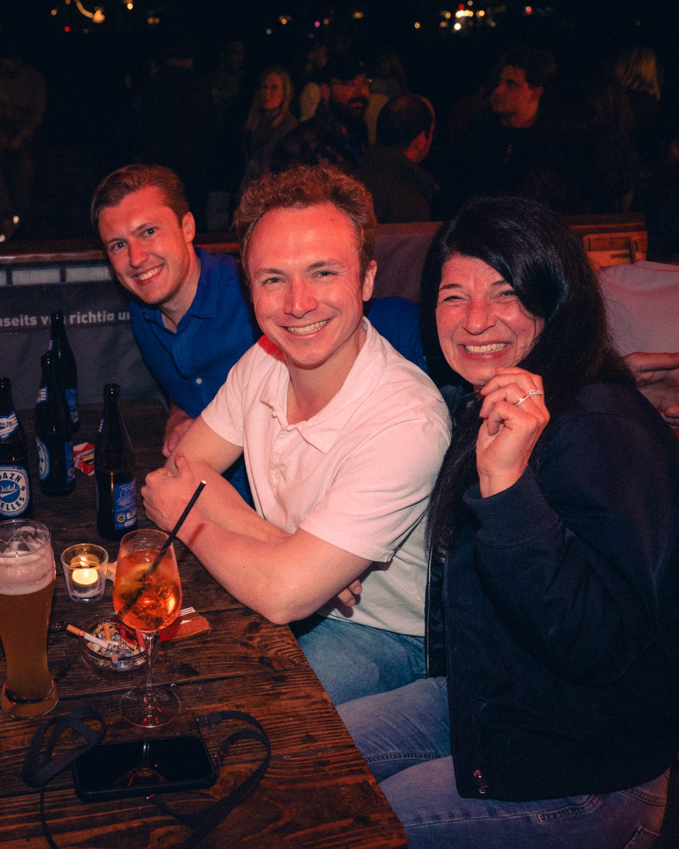 Drei gut gelaunte Gäste am Tisch mit Boazn Helles und Aperol Spritz – Boazn an der Isar, Bar in München, Mai 2026 5