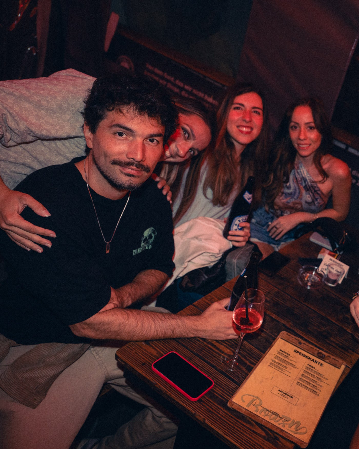 Mann und drei Frauen kuscheln eng am Tisch, Wein und Bier vor sich – Boazn München, Tanzbar an der Isar, Mai 2026 7