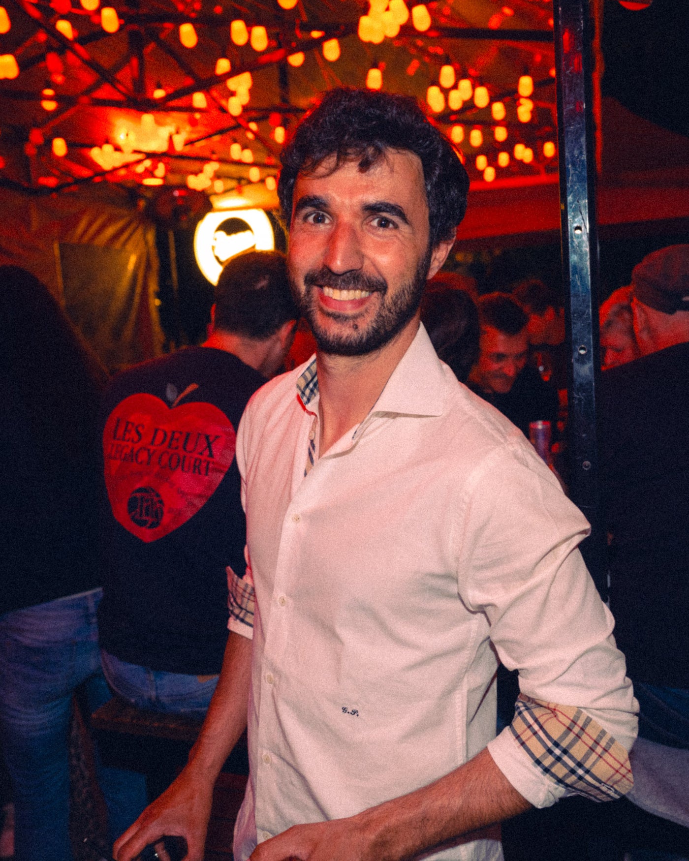 Mann im weißen Hemd lacht herzlich unter rotem Lichtervorhang – Boazn an der Ludwigsbrücke, Bar in München, Mai 2026 10