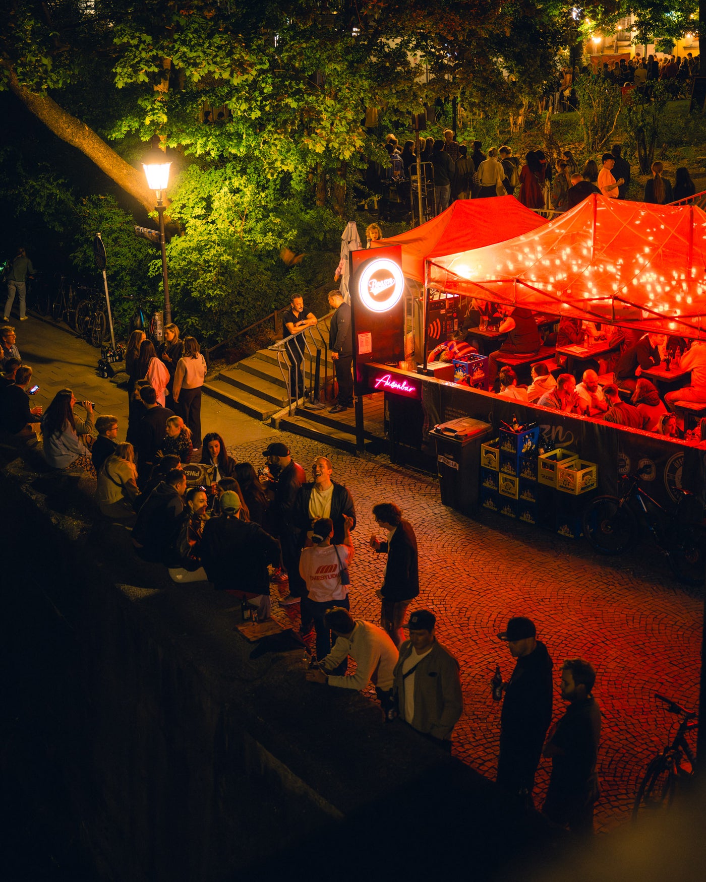 Blick von oben auf den roten Boazn-Pavillon mit Gästen vor dem leuchtenden Schild – Boazn an der Ludwigsbrücke, Nightlife München, Mai 2026 18