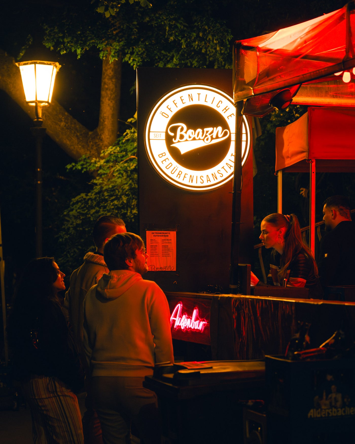 Boazn-Leuchtschild mit pinker Anstalt-Neon und Aigner-Bier-Hinweis am Outdoor-Tresen – Boazn München, Kneipe an der Isar, Mai 2026 19
