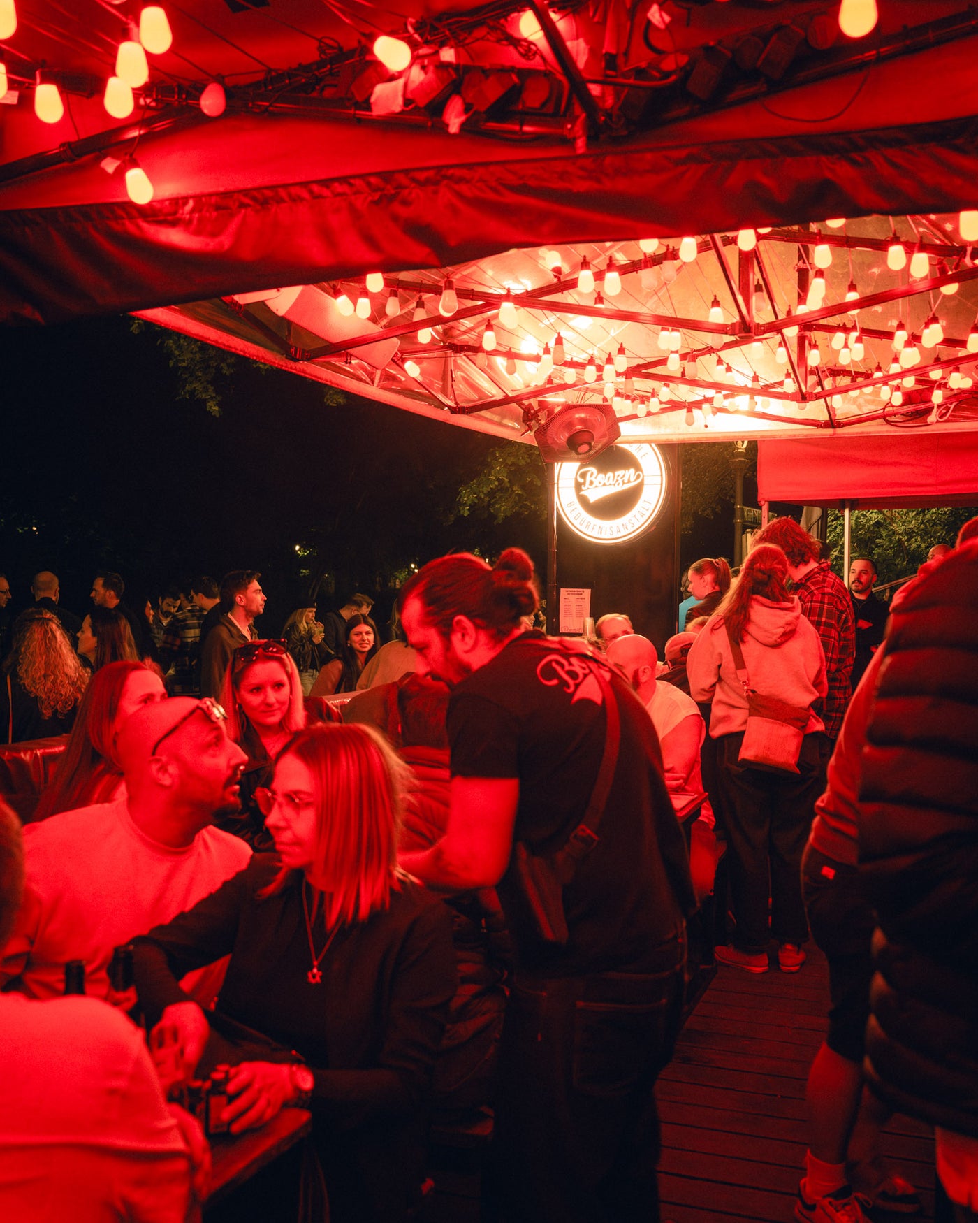 Gäste im roten Licht der Boazn-Pavillons feiern entspannt draußen – Boazn an der Ludwigsbrücke, Bar in München, Mai 2026 22