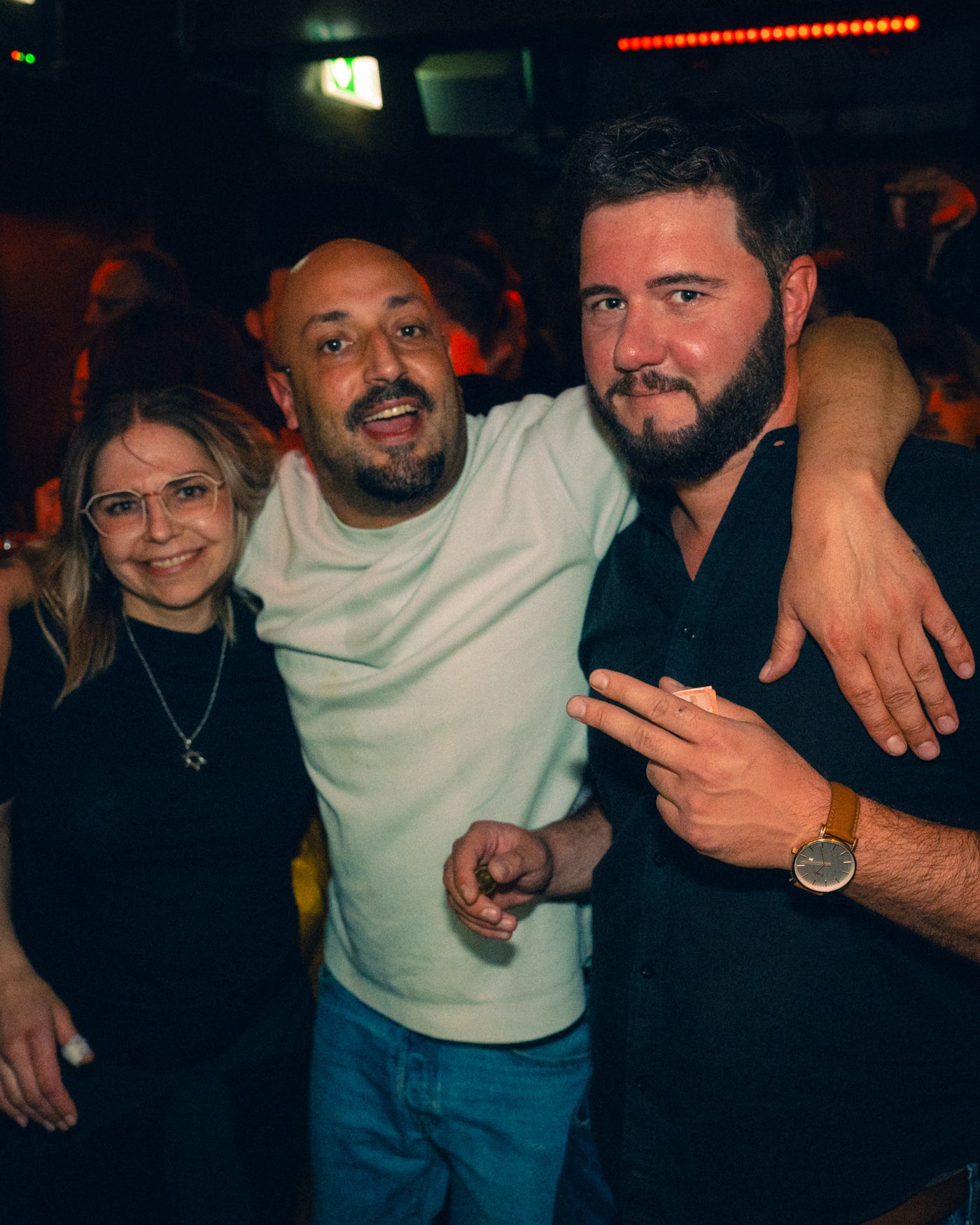Drei Freunde Arm in Arm mit breitem Grinsen unter warmem Licht – Boazn München, Bar an der Ludwigsbrücke, Mai 2026 34