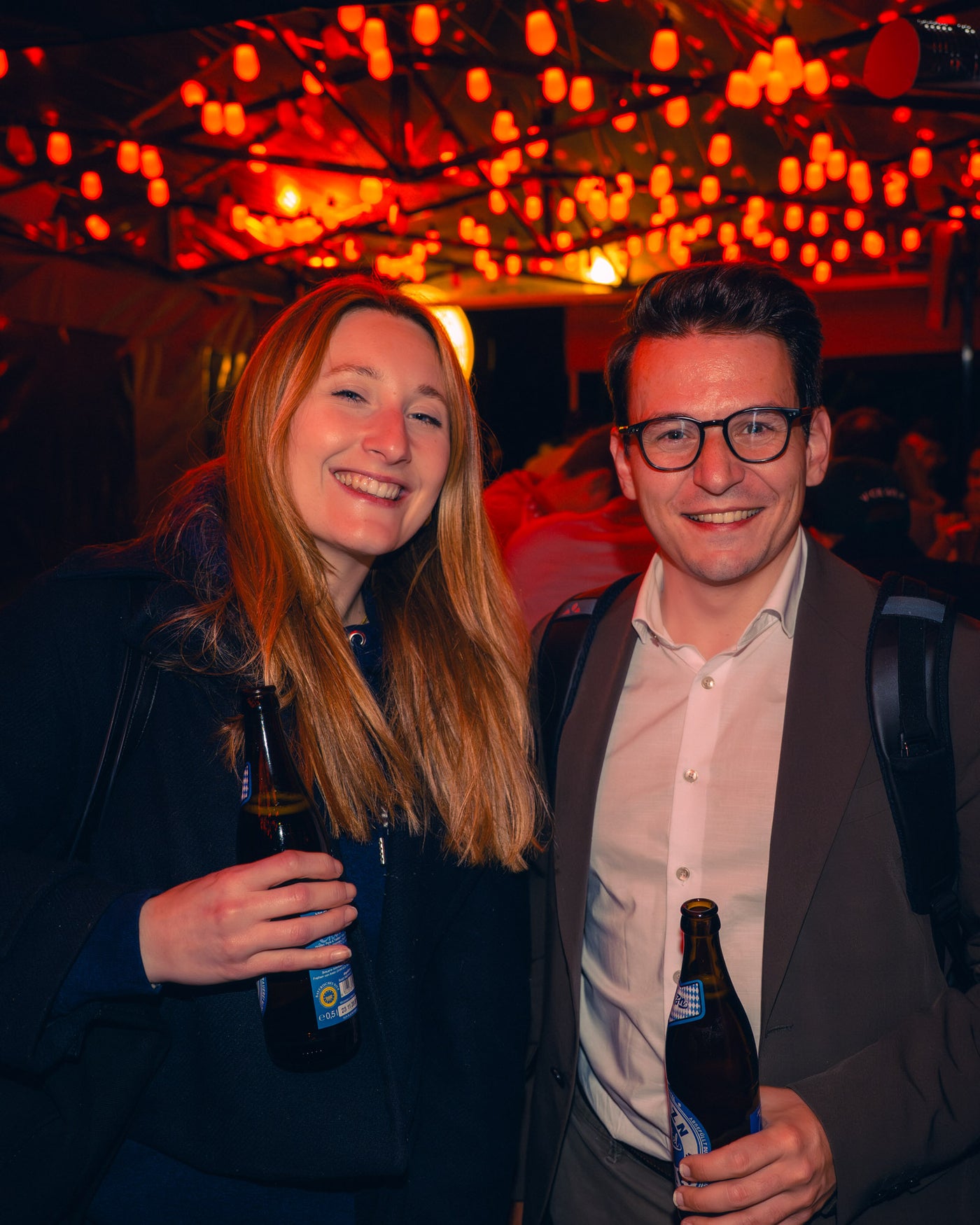 Pärchen strahlt mit Eigenbier-Flaschen unter dem roten Lichterhimmel – Boazn München, Bar an der Isar, Mai 2026 41